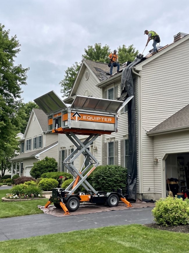 Roofers sending old shingles into a raised Equipter container